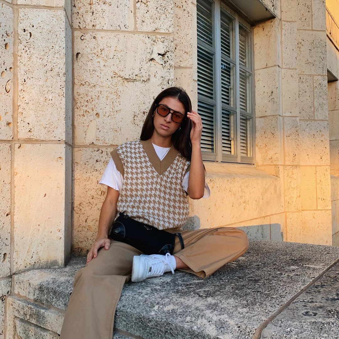 Woman wearing beige and white sweater vest with t-shirt and trousers