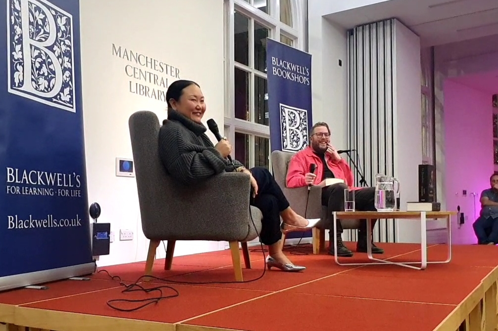 Hanya Yanagihara and Simon Savidge sitting on armchairs on a stage in the Manchester City Library