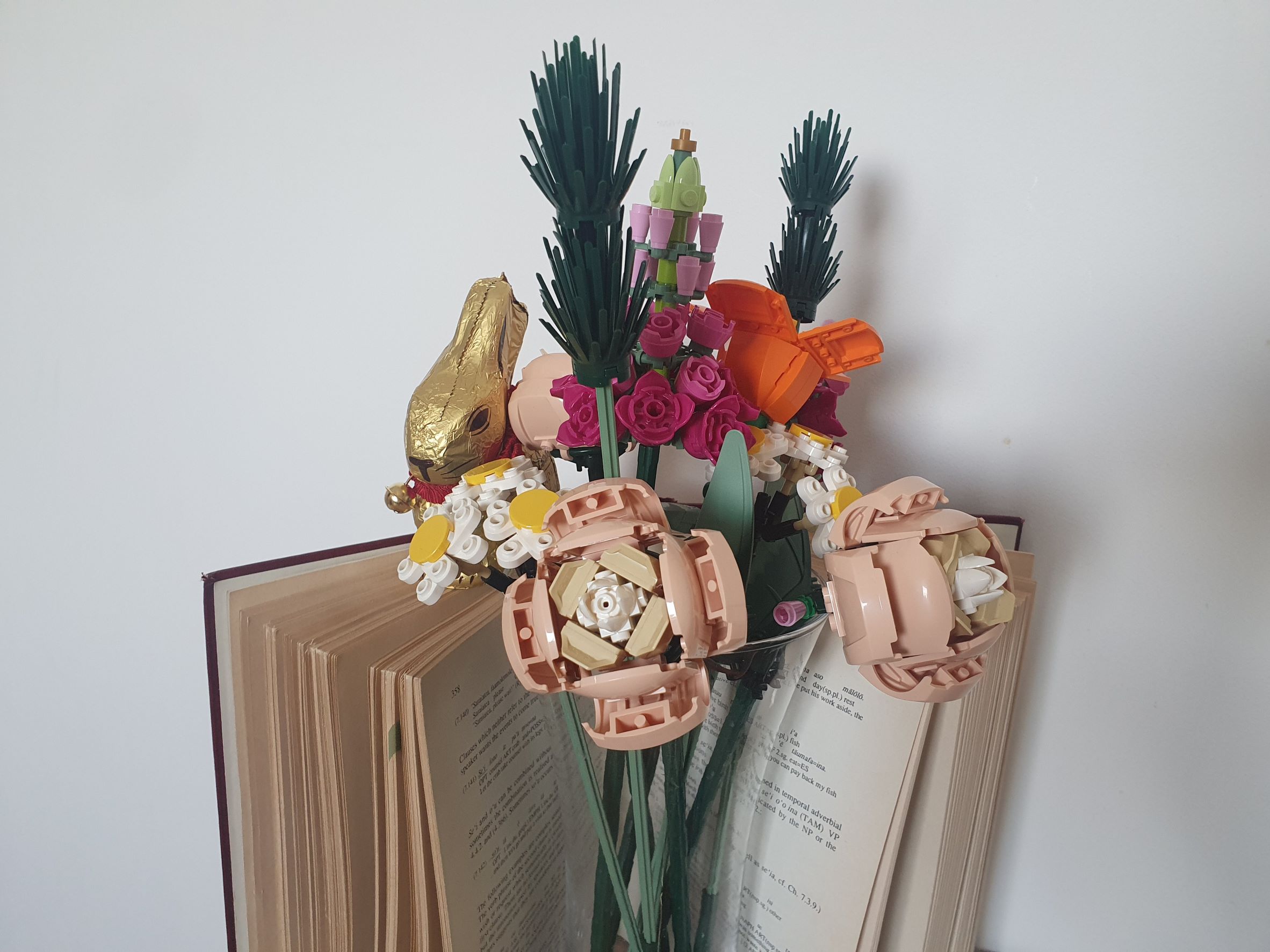 An opened grammar book with a transparent vase of Lego flowers in front of it and a slightly hidden chocolate bunny
