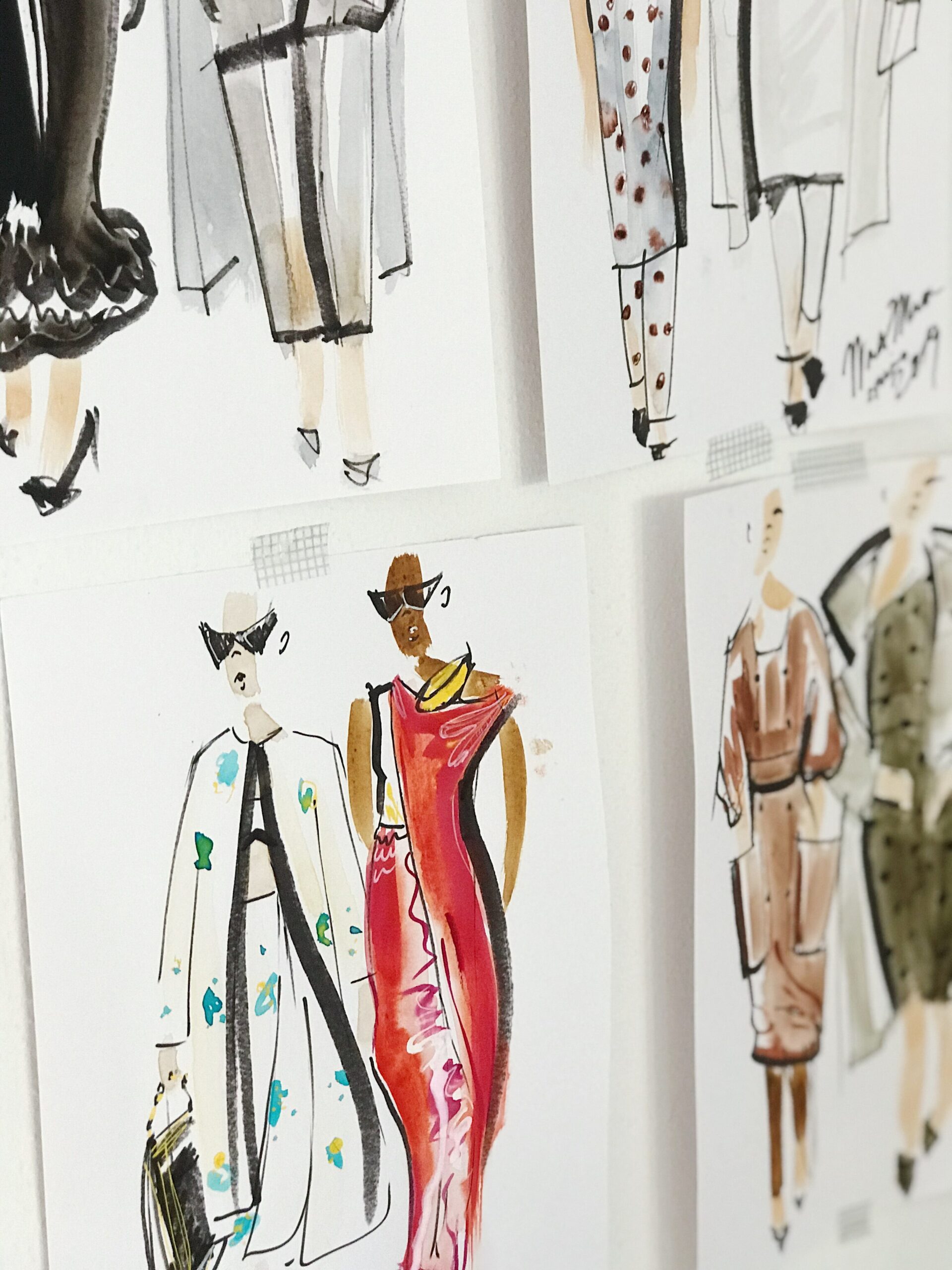 Fashion sketches stuck on a wall with a close-up of one showing a red dress and another showing a blue and white outfit