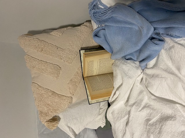A bed with blankets and a scarf, with a book in the centre