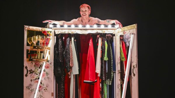 Luke Hereford leans over the top of a wardrobe full of dresses and topped with bulb lights