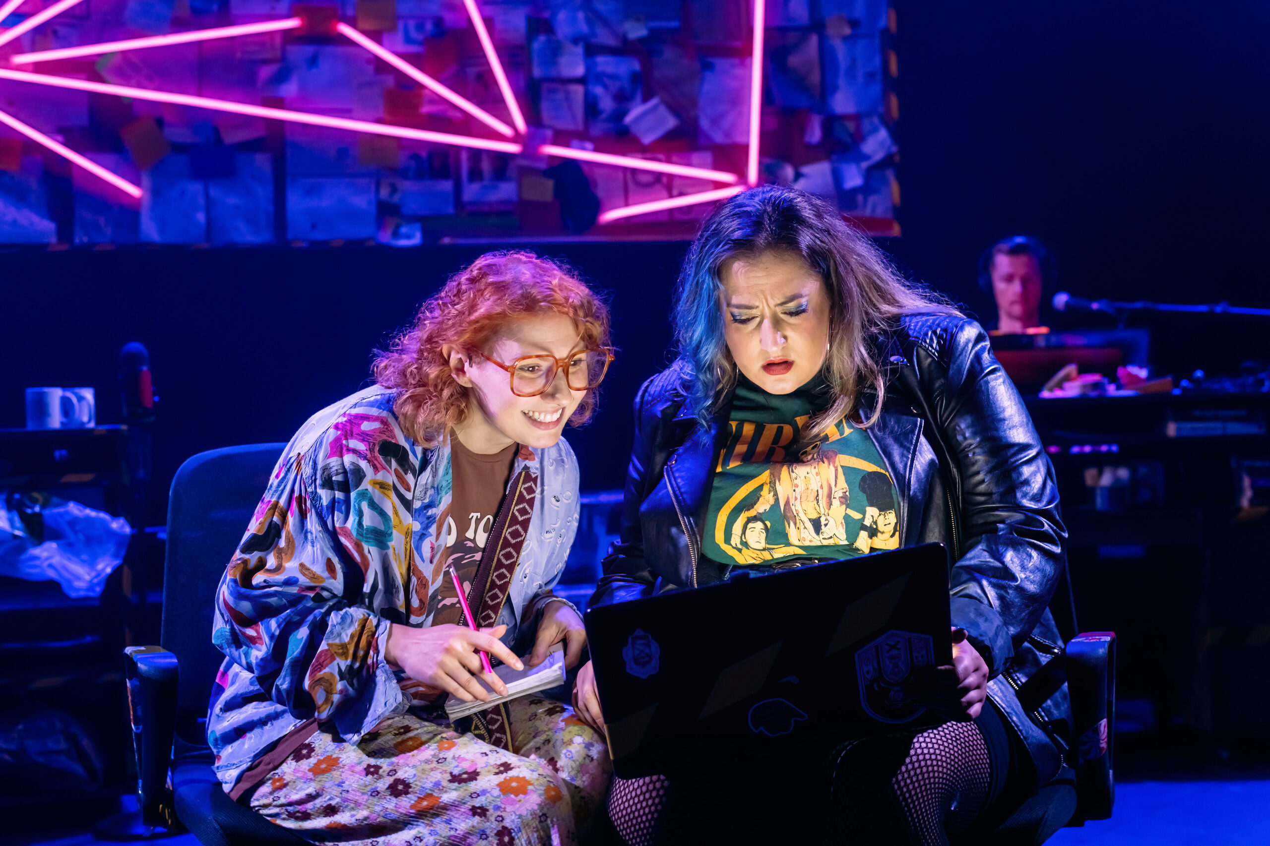 Intrigued, Kathy and Stella look at a laptop perched on their knees, with a notebook and pencil ready. Pink and purple laser lights fill the background.