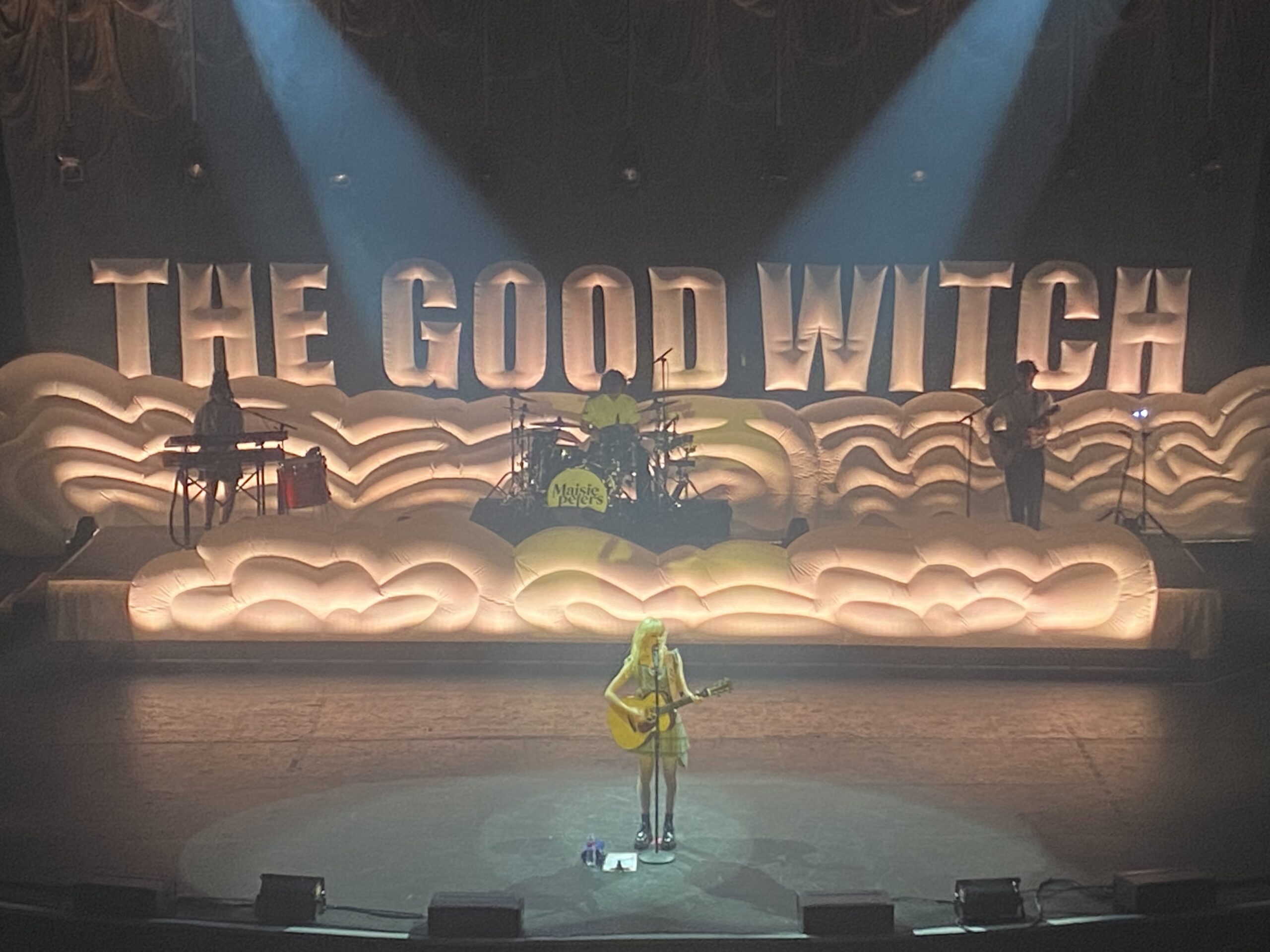 Maisie Peters on stage in front of The Good Witch sign