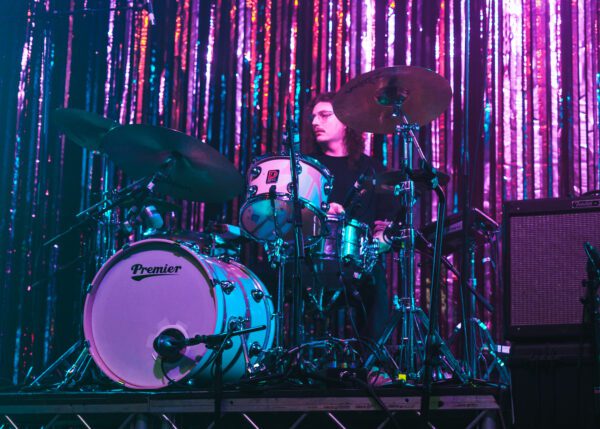 Haydn Evans plays drums in front of a wall of tinsel.