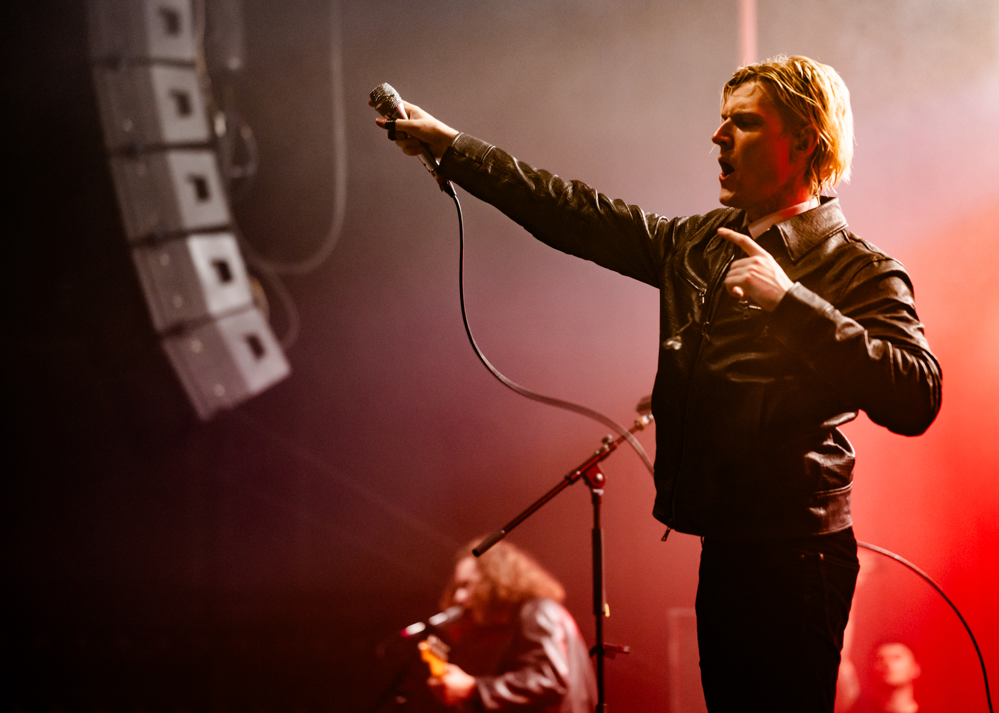 Oscar Pollock from Sundara Karma punches the air with his mic in hand, mouth open in a yell.