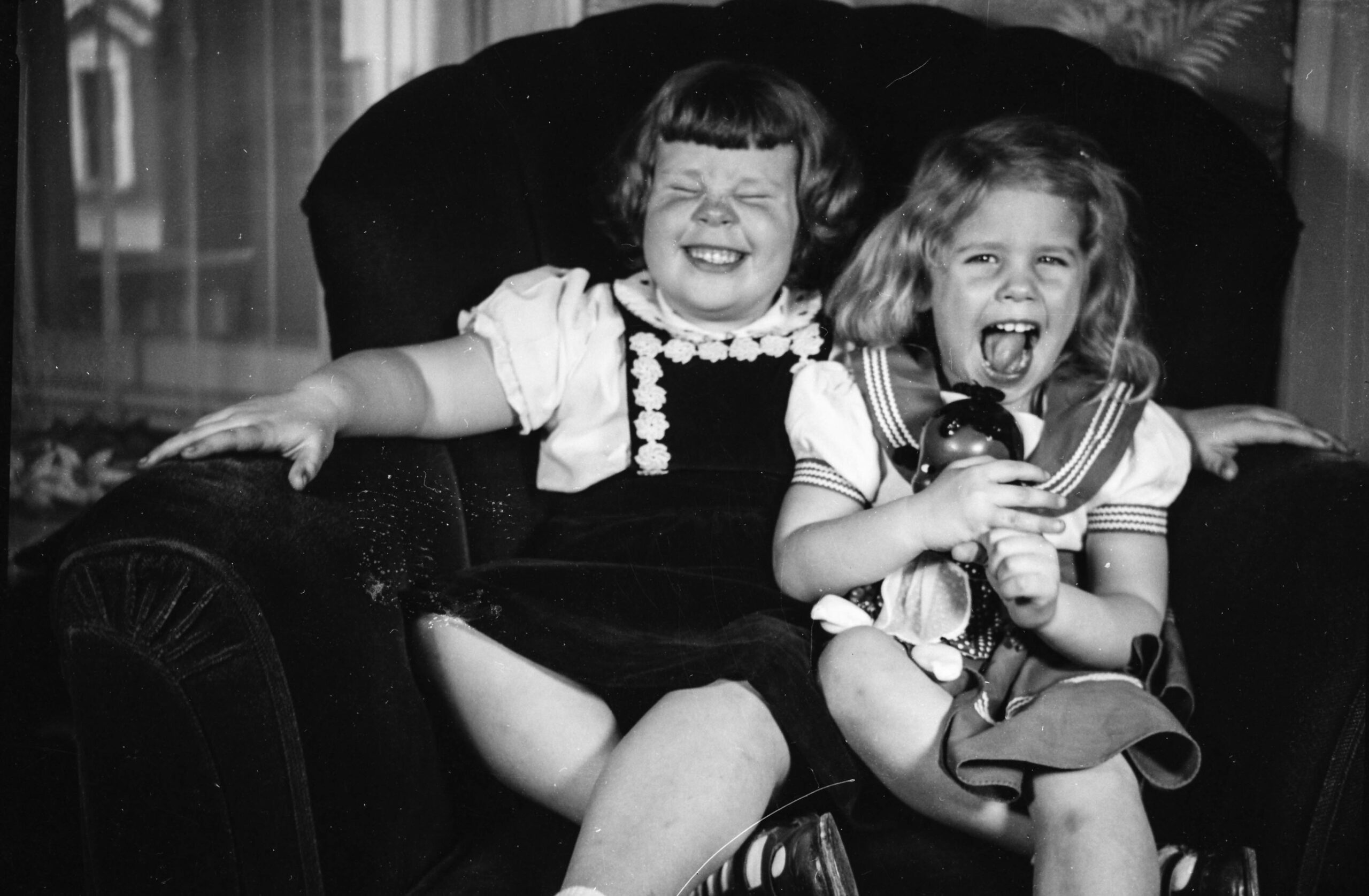 Two little girls laughing on a  sofa