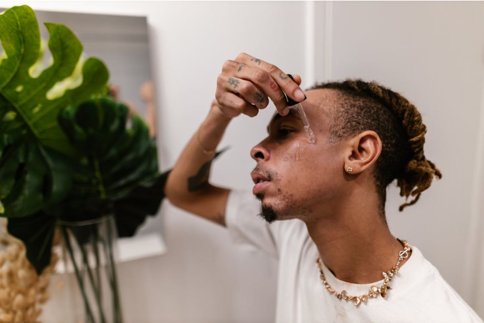 Man doing skincare in white bathroom with green plant in background for Conversations about acne article