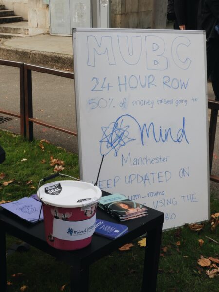 A sign advertising the 24 hour row, with a bucket for donations