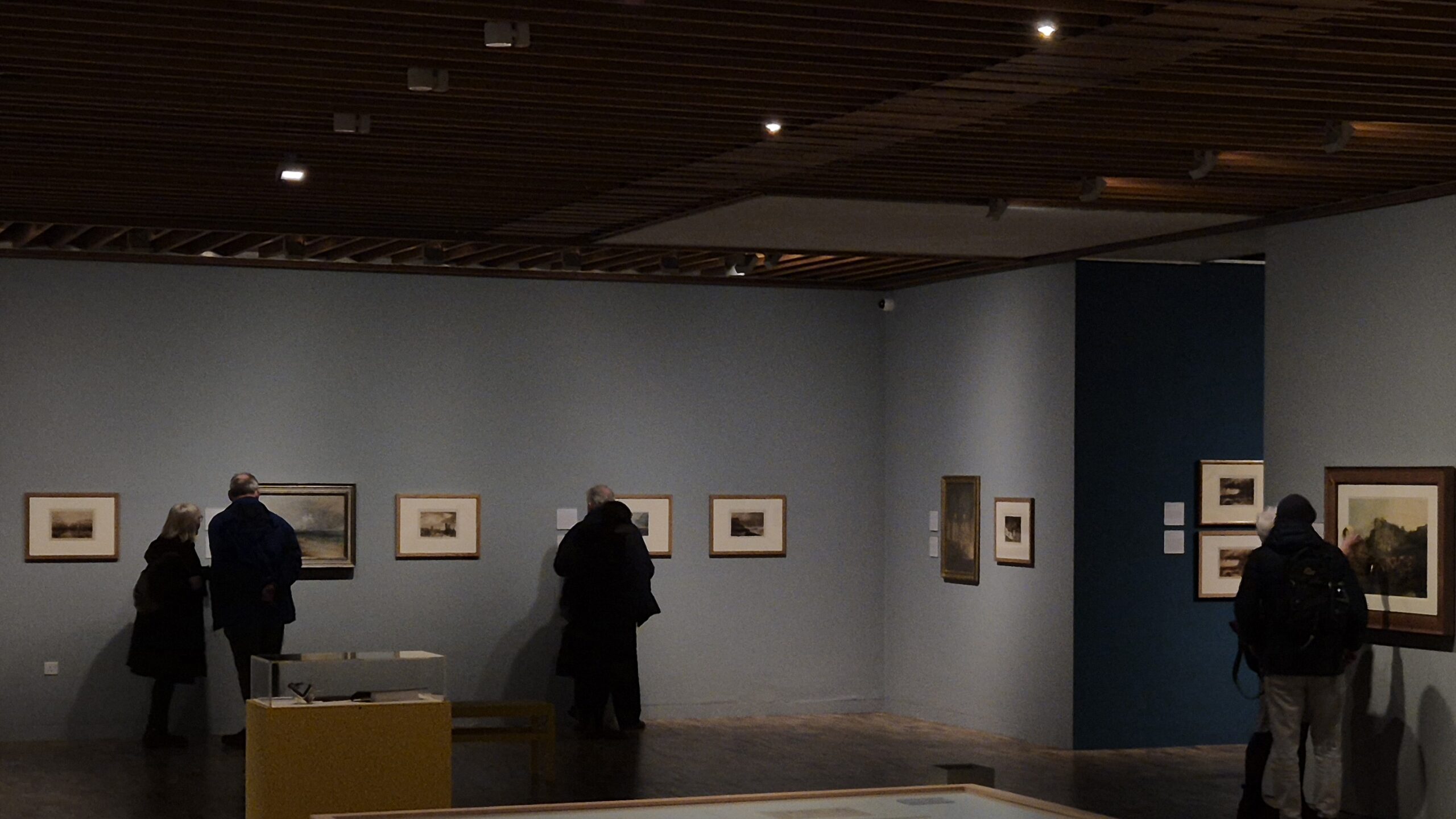 A room of an art gallery with visitors looking at the art