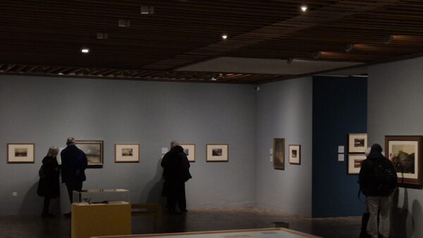 A room of an art gallery with visitors looking at the art