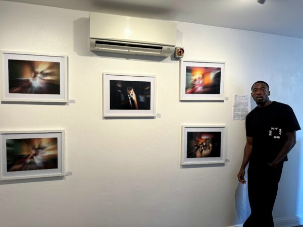 Photographer standing next to 5 pictures, against a wall