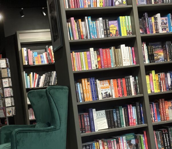 Rows of books line the walls of Queer Lit. A green armchair sits in the foreground.One of the 6 best bookshops and libraries in Manchester.