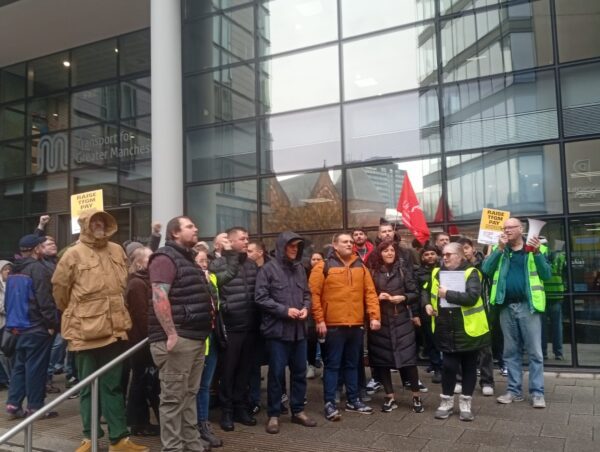 A group of striking workers outside an office building, some holding flags and signs.