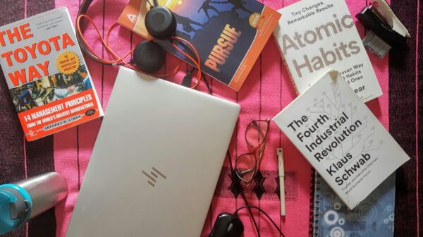 A desk full of books, headphones, a flask, and a computer.